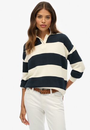 Navy and cream striped knit pullover with a collared neckline, three-button detail, and loose fit. Paired with white pants and a braided belt.
