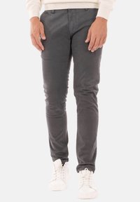 Pantaloni slim-fit grigi scuri in cotone con una texture liscia, dotati di tasche frontali e chiusura con bottone, abbinati a sneakers bianche.