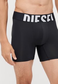 Boxer-briefs noirs avec une large ceinture élastique portant le mot "DIESEL" en blanc. Le tissu est lisse et moulant.