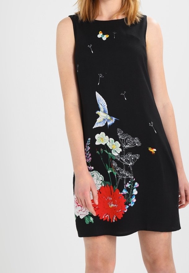 Robe noire sans manches avec des imprimés colorés de fleurs, oiseaux, papillons et abeilles sur le devant, portée par une femme debout.