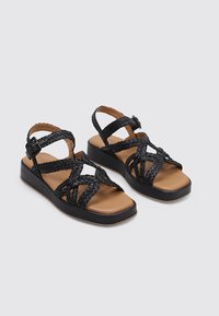 Sandalias de cuero trenzado negro con suela plana y plantilla acolchada. Cuenta con correas ajustables y un diseño de talón cerrado.