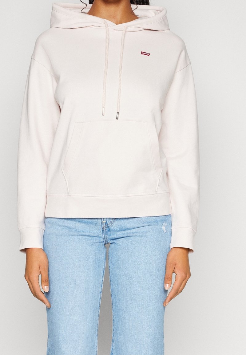 Sweatshirt à capuche rose clair avec une poche frontale, un col à cordon et un petit logo rouge Levi's. Associé à un jean bleu clair.
