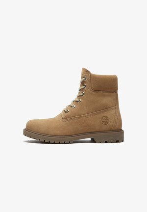 Lichtbruine suède veterlaars met een gewatteerde kraag, een robuuste zool en een geperst Timberland-logo aan de zijkant, weergegeven in profiel.