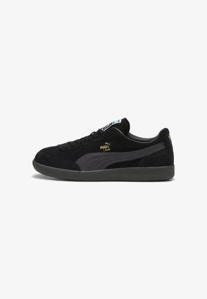 Zapatilla Puma de ante negro de perfil bajo con una franja gris oscuro, suela negra y el logo dorado "Puma Liga" en el lateral, vista desde el lado izquierdo.
