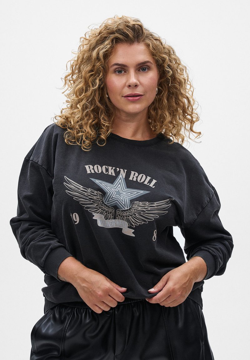 Čierna mikina s dlhými rukávmi, s grafikou hviezdy a krídla, textom "ROCK'N ROLL" a voľným strihom, skombinovaná s čiernymi lesklými šortkami.