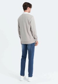 Felpa grigia chiaro con colletto bianco, vestibilità comoda, maniche lunghe e polsini a costine, abbinata a jeans blu scuro e sneakers bianche.