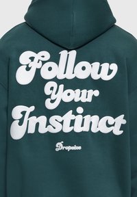 Sweat à capuche vert foncé avec grand texte blanc "Follow Your Instinct" et plus petit "Dropsize" imprimés au dos.
