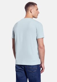 Světle modré tričko s krátkým rukávem vyrobené z měkké tkaniny s uvolněným střihem. Zadní strana má hladkou texturu a klasický kulatý výstřih.