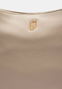 Borsa a tracolla in pelle beige con texture liscia e logo interlocking dorato vicino al centro in alto.