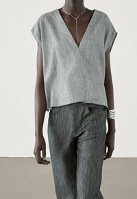 Gray, short-sleeved wrap top with a V-neckline, paired with dark gray, slim-fit jeans. Silver bracelet accent on the wrist.