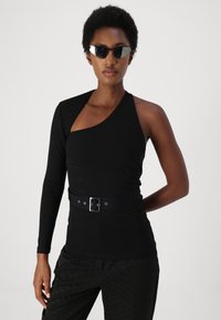 Top negro de manga larga con escote asimétrico, diseño ajustado y un cinturón negro ancho con hebilla plateada. Combinado con pantalones negros de estampado.