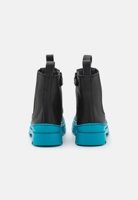 Bottes de cheville en cuir noir avec une semelle en caoutchouc turquoise. Les caractéristiques incluent des tirettes doubles et une texture lisse.