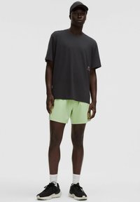Tricou negru cu mânecă scurtă, pantaloni scurți verzi deschis, șosete albe și pantofi sport negri. Design simplu, croială lejeră și textură moale.