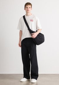 Tricou alb din bumbac cu logo-ul roșu "Calvin Klein", pantaloni largi negri și o geantă de umăr neagră, matlasată. Adidași albi completează ținuta.
