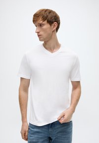 Λευκό βαμβακερό T-shirt με κοντά μανίκια και V λαιμόκοψη, φορεμένο με μπλε τζιν παντελόνι· λεία υφή, άνετη εφαρμογή, μινιμαλιστικός σχεδιασμός, χωρίς σχέδια ή διακοσμήσεις.