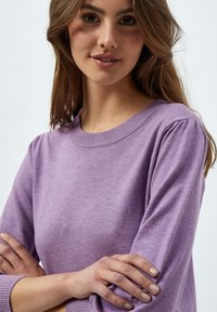 Lila gestrickter Pullover mit rundem Ausschnitt, langen Ärmeln und subtilen Puff-Schulterdetails. Weicher Stoff und gleichmäßiges Strickmuster.