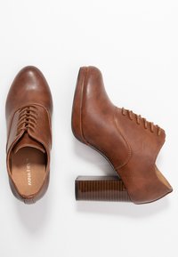 Scarpe in pelle marrone con punta rotonda, design con lacci e tacco quadrato testurizzato. La parte superiore presenta dettagli lisci e cuciture.