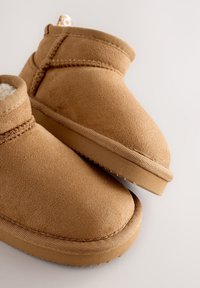 Bottines en daim couleur camel avec doublure douce, dotées d'un bout arrondi et d'une semelle en caoutchouc texturée. Les accents incluent des détails de couture sur la tige.