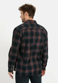 Sort og rød ternet flannel skjorte med lange ærmer, der har knapmanchet og klassisk krave, vist fra ryggen.