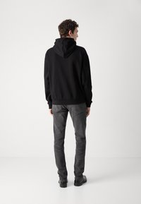 Sudadera negra con capucha y bolsillo tipo canguro, combinada con jeans grises. La tela parece suave; la silueta es relajada y casual.