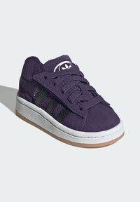 Ljubičaste suede tenisice s crnim bočnim trakama, bijelim gumenim đonom i odgovarajućim ljubičastim vezicama. Istaknut logotip na jeziku.