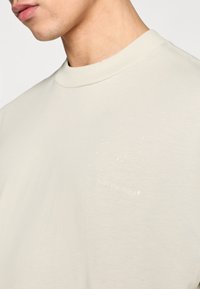 Ανοιχτό γκρι βαμβακερό T-shirt με υφή, που διαθέτει στρογγυλή λαιμόκοψη και ένα διακριτικό εκτυπωμένο σύνθημα, «τρέξε με το μυαλό», στο μπροστινό μέρος.