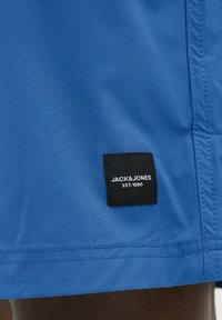Koninklijk blauwe shorts met een gladde textuur, voorzien van een zwart label met witte tekst ("JACK & JONES EST.1990") genaaid aan de zijkant.