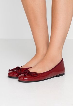 Czerwone lakierowane baleriny mają okrągły czubek i dekoracyjną kokardę z plecionej liny z przodu. Podeszwa jest płaska i czarna.