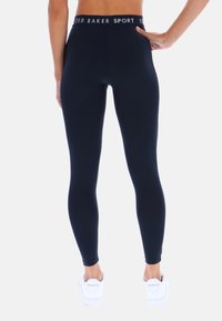 Granatowe legginsy z wysokim stanem z białym logo "TED BAKER SPORT" na pasie, wykonane z gładkiej, elastycznej tkaniny i o dopasowanym kroju.