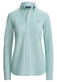Chemise bleu clair à manches longues, avec un col, fabriquée dans un tissu texturé, comportant un petit logo sur la poitrine.