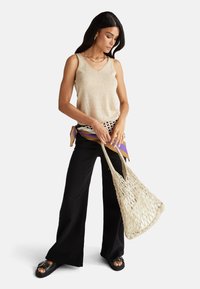 Béžový top bez rukávů, široké černé kalhoty a pletená krémová taška. Top má výstřih do V; souprava obsahuje jemnou šálu jako akcent.