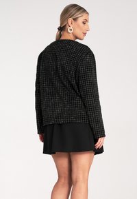 Czarna kurtka o teksturowanej powierzchni z wzorem w kratę, charakteryzująca się luźnym krojem i długimi rękawami, zestawiona z czarną spódnicą. Wykonana z miękkiego, tkane materiału.