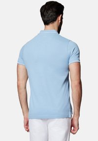 Jasnoniebieska koszulka polo wykonana z gładkiego materiału, z kołnierzykiem i krótkimi rękawami. Widok z tyłu podkreśla szwy i detale logo.