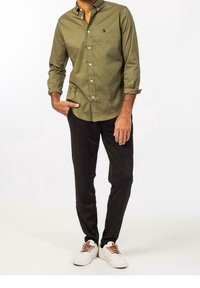 Olivgrön skjorta med knappar och långa ärmar, kombinerad med svarta slim-fit byxor och vita sneakers med bruna snören.