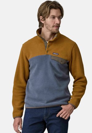 Suéter de forro polar en marrón y azul, con cuello, cierre de botones y bolsillo en el pecho; textura suave y bloques de color contrastantes.