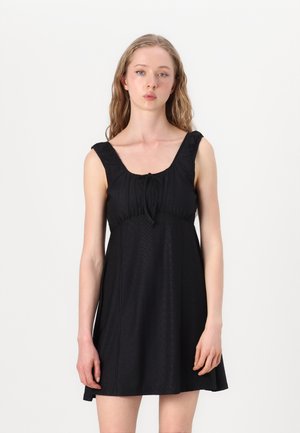 Abito nero senza maniche con scollatura quadrata, spalline arricciate, tessuto texture e un laccio regolabile sul petto. Forma ad A, lunghezza ginocchio.