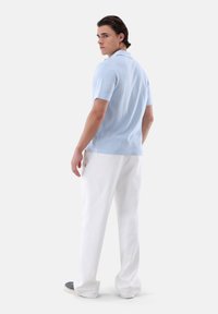 Polo shirt azzurro, a maniche corte, con dettagli del colletto, abbinato a pantaloni bianchi a gamba larga e scarpe grigie. Elementi di design semplici e puliti.