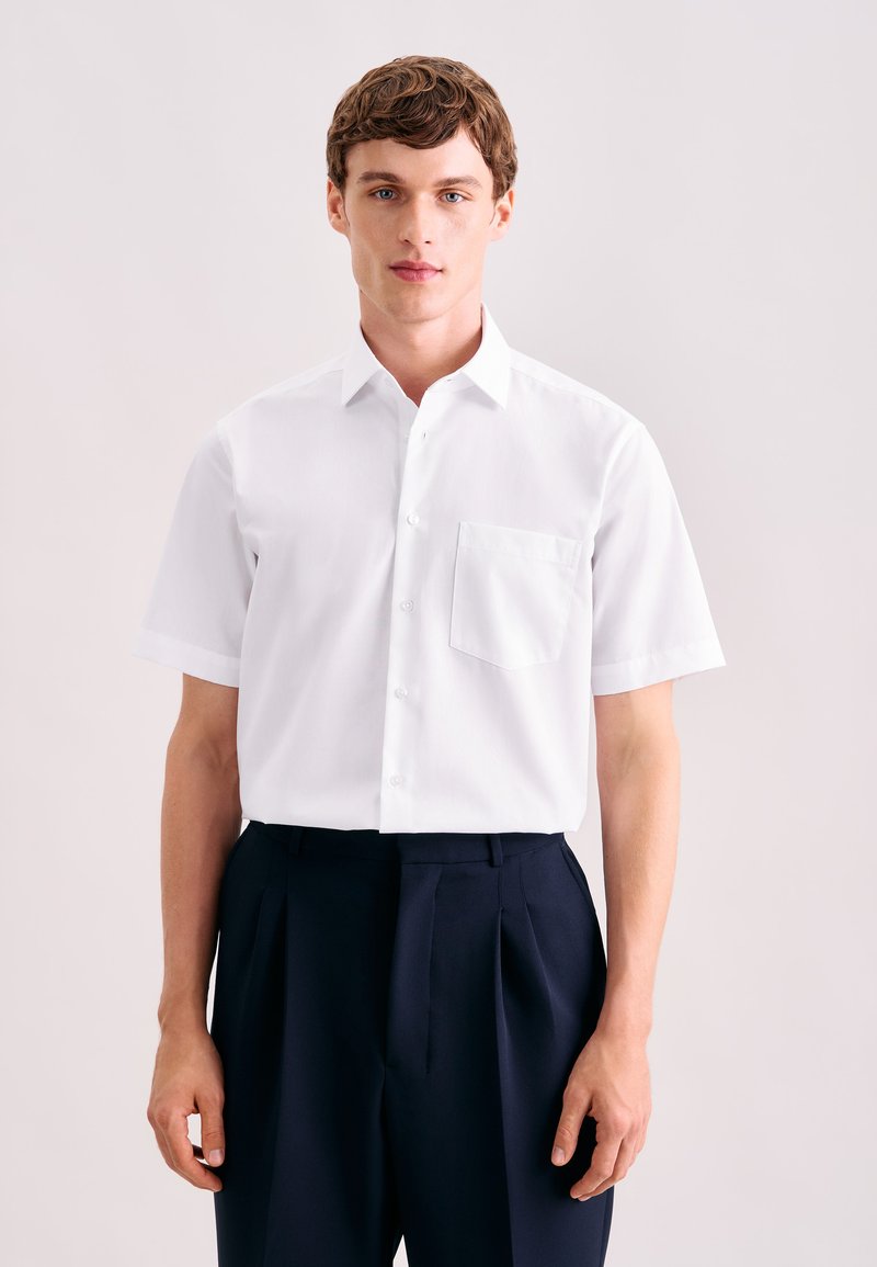 Wit overhemd met korte mouwen, een sluiting met knopen, een borstzakje en een puntige kraag, gedragen met donkerblauwe broek.