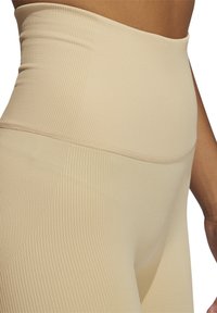 Leggings beige a vita alta realizzati in tessuto a coste, con una texture liscia e un bordo contornato per un supporto aggiuntivo.