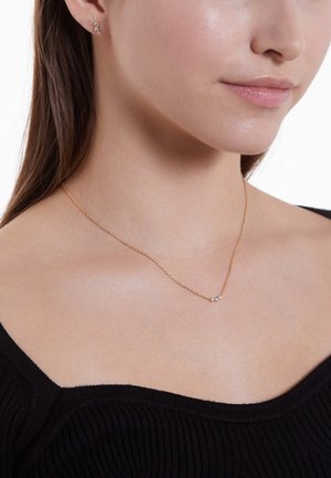 Gouden ketting met een delicate ketting, voorzien van kleine heldere edelstenen. Draag met bijpassende stud-oorringen. Getextureerde zwarte top.