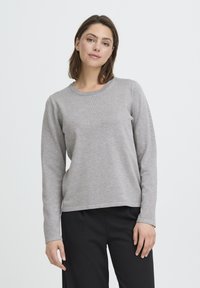 Chemise à manches longues gris clair avec un col rond lisse et une encolure discrètement côtelée, associée à un pantalon noir. Design simple et polyvalent.