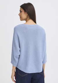 Gaiši zils adīts džemperis ar brīvu piegriezumu, plašu laivu formas apkakli un trīs ceturtdaļu piedurknēm, ar teksturētu rakstu un noapaļotu apakšu.