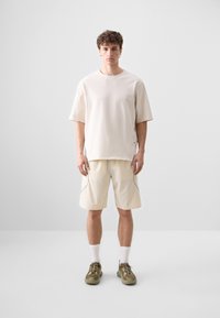 Beige cotton t-shirt with a relaxed fit, paired with light beige, knee-length shorts featuring a subtle textured pattern and gray accents.