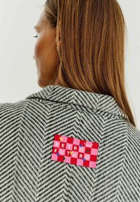 Sako šedé barvy s vzorem houndstooth, s červenou a růžovou kostkovanou nášivkou s nápisem "RETRO FUTURO", zdobené barevnými srdci a akcenty.