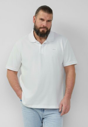 Weiße Poloshirt aus Baumwolle mit klassischem Kragen, kurzen Ärmeln und kleinem Logo auf der Brust. Getragen mit hellblauen Jeans.