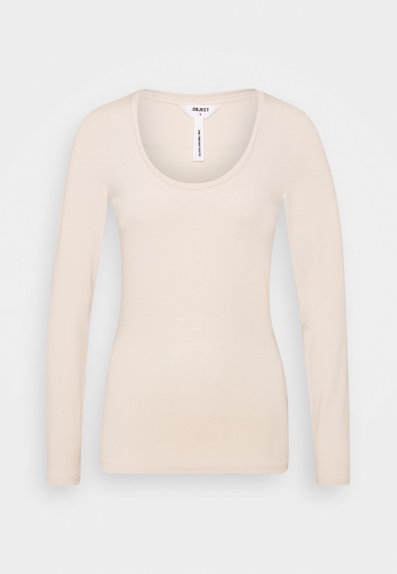Chemise beige ajustée à manches longues avec encolure dégagée, taille petite, présentée sur fond uni gris clair.