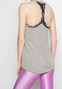 Camiseta deportiva gris con diseño de espalda nadadora y detalles de correas negras, combinada con leggings púrpuras brillantes. Textura suave en toda la prenda.