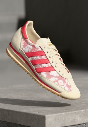 Adidas sneakers met een bloemmotief in roze en wit, crème leren overlays, rode accenten en een gumrubberen zool. Klassiek retro ontwerp.