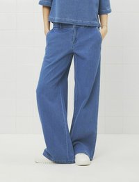 Ljust blå vida jeans med hög midja, framfickor och lös passform. Kombinerat med vita sneakers.