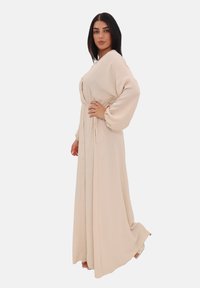 Robe longue crème avec une taille cintrée, un devant à boutons et des manches bouffantes, conçue dans un tissu lisse, longueur cheville avec des drapés doux.